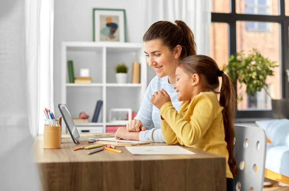 A mother and her daughter sitting together at a table at home, working on an activity